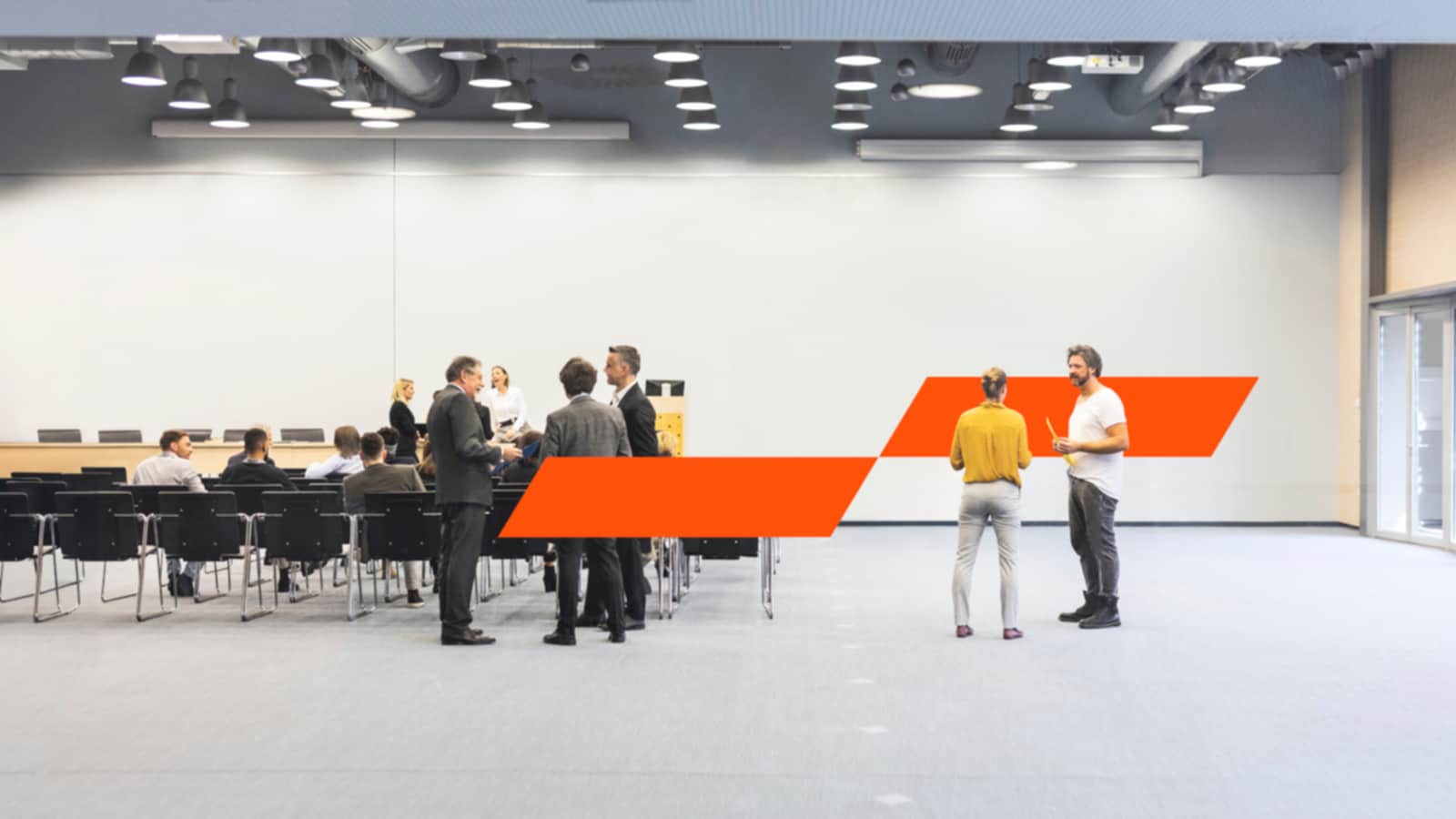 Kontoriruum inimestega laua ääres istumas ja püsti seismas, kaks kolleegi teistest eraldi püsti seistes arutamas