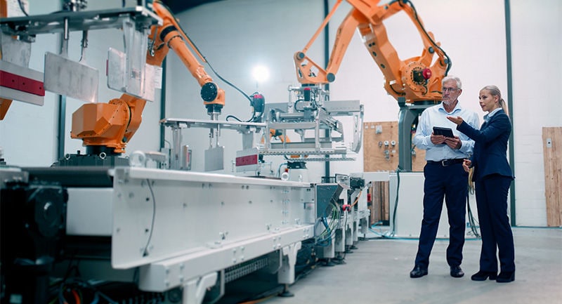 Two co-workers having a discussion in a factory with robotic arms
