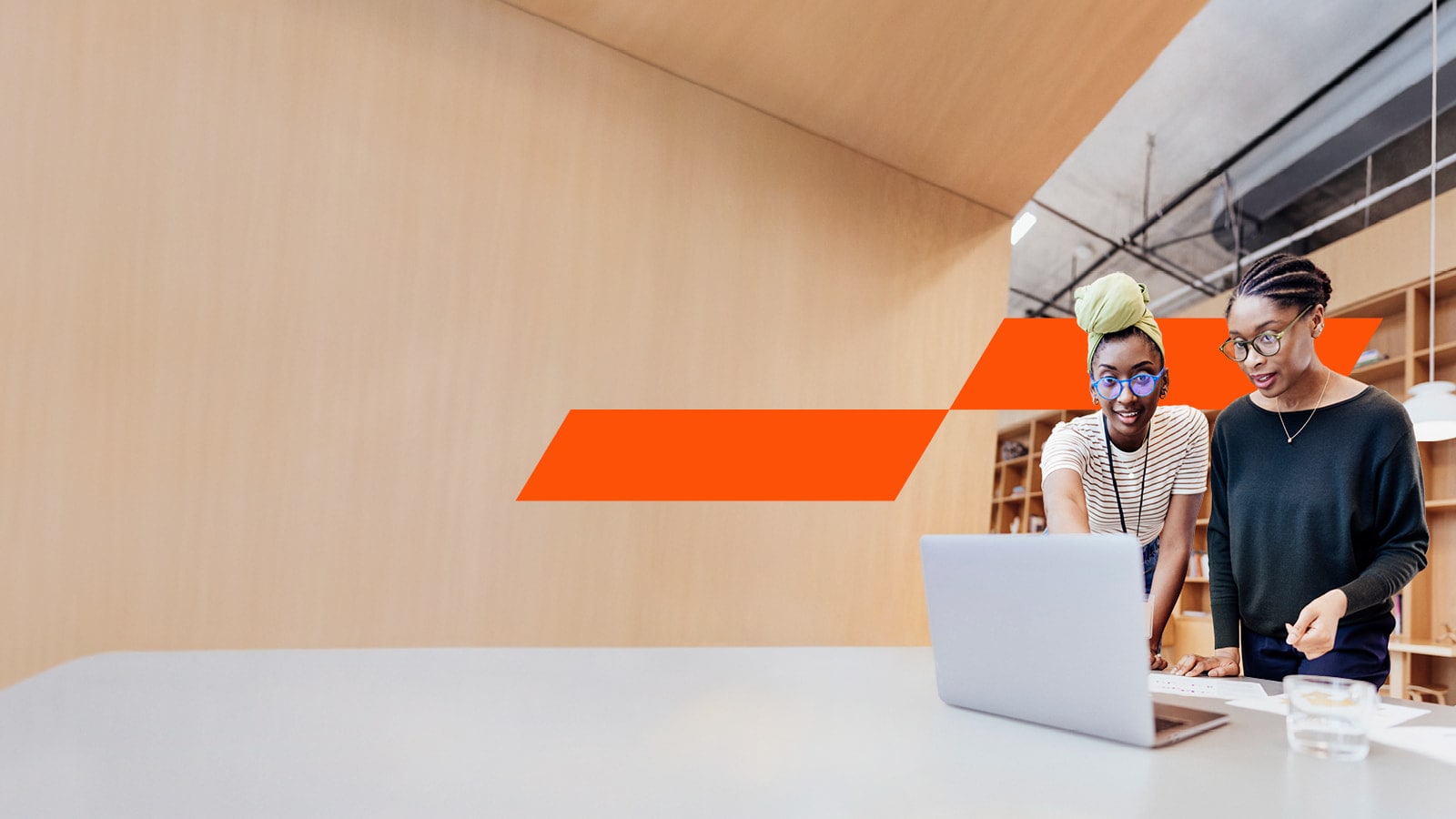 Two professional women working on a laptop in a meeting room with wood walls