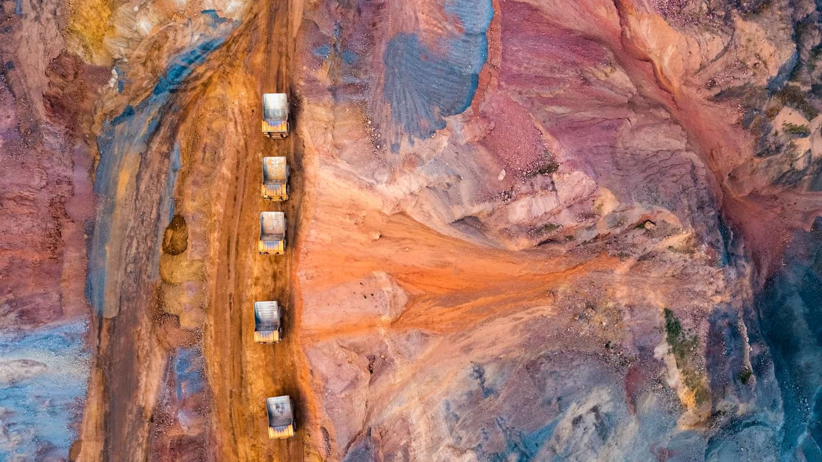 Aerial view of trucks and machinery operating in a colorful open-pit mine.