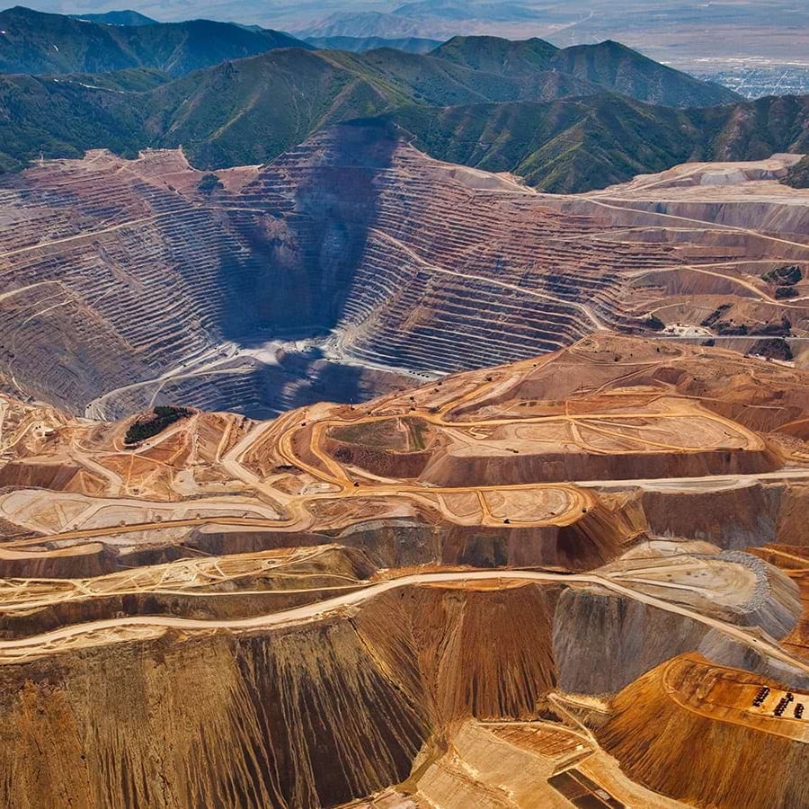 Aerial view of a large open-pit copper mine with terraced layers and surrounding mountains.