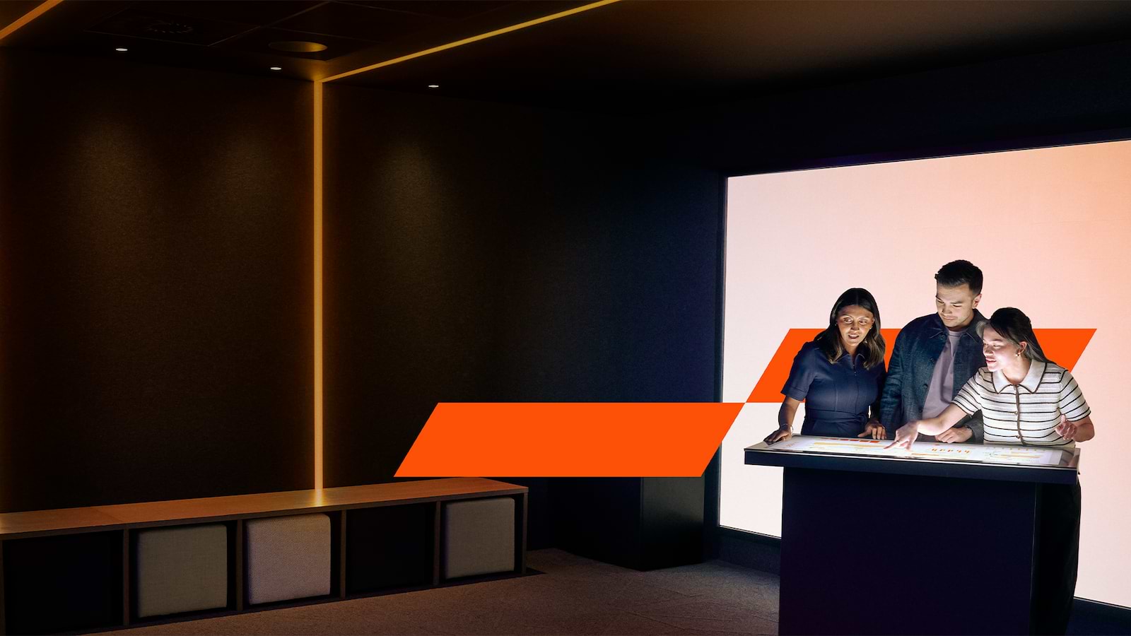 Three diverse professionals collaborate in a modern tech office using a large touch-screen device. 