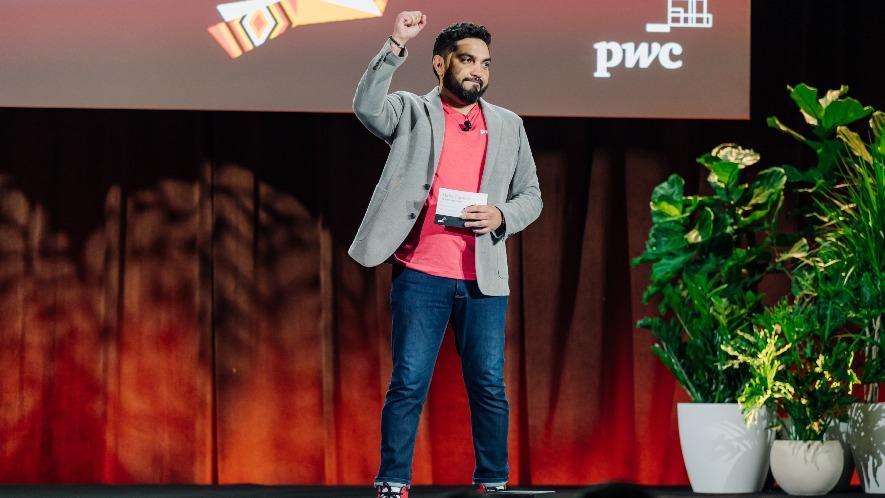 Image shows a male speaker on stage at a PwC Thrive Together event holding a speaker note card in his left hand and his right hand in a fist raised in the air.