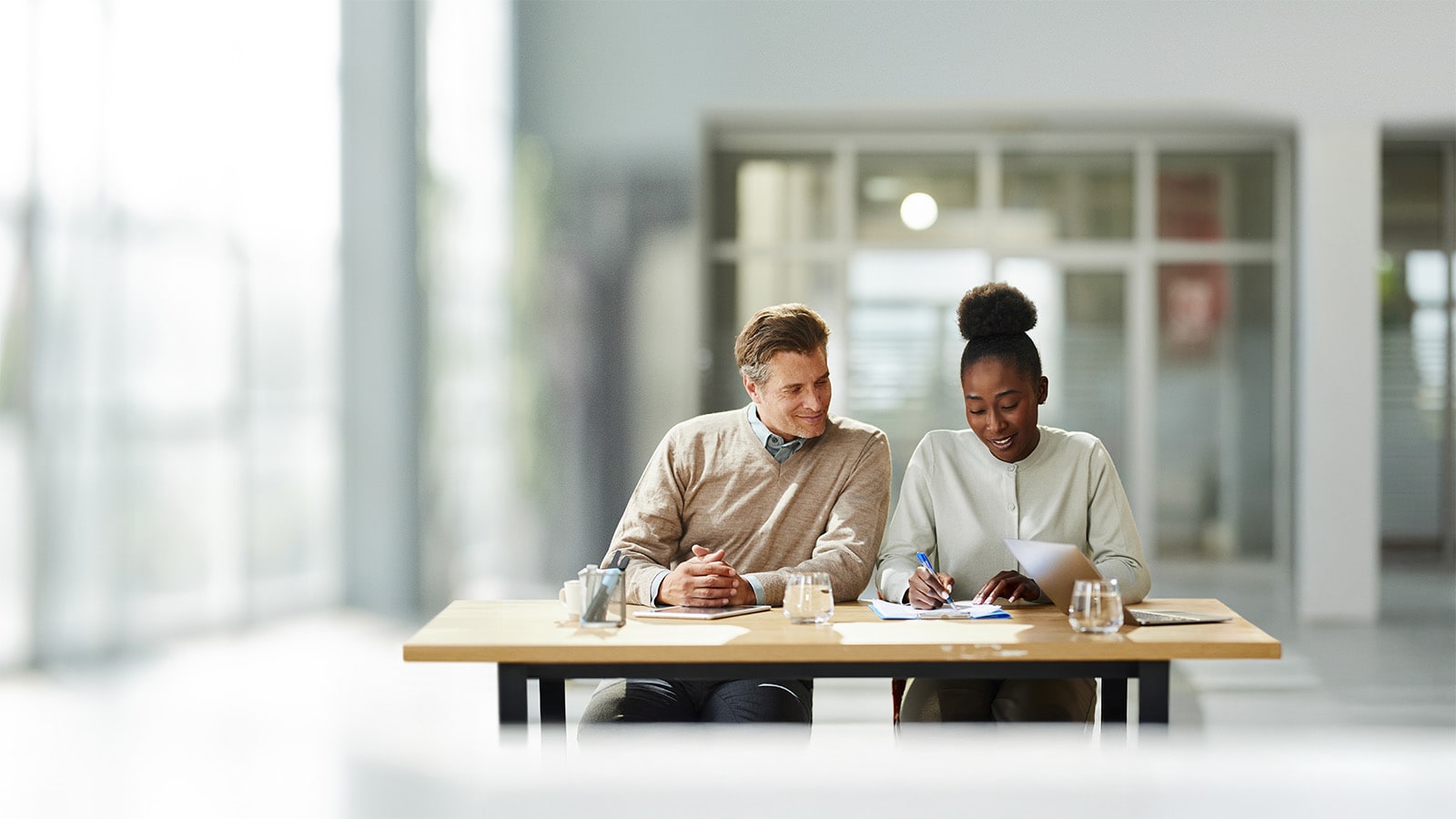 A male and female colleague sitting at an office desk looking at a document