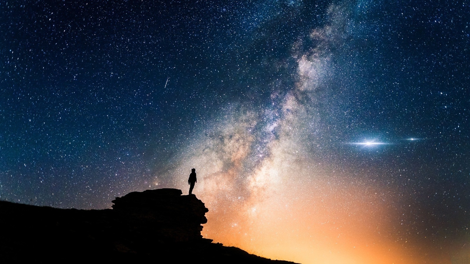 Man on cliff looking at stars and sky