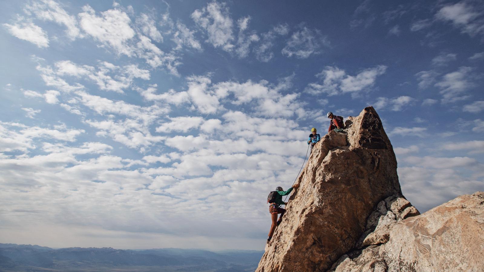 Three rock climbers each the summit of a mountain in Tetons, Wyoming