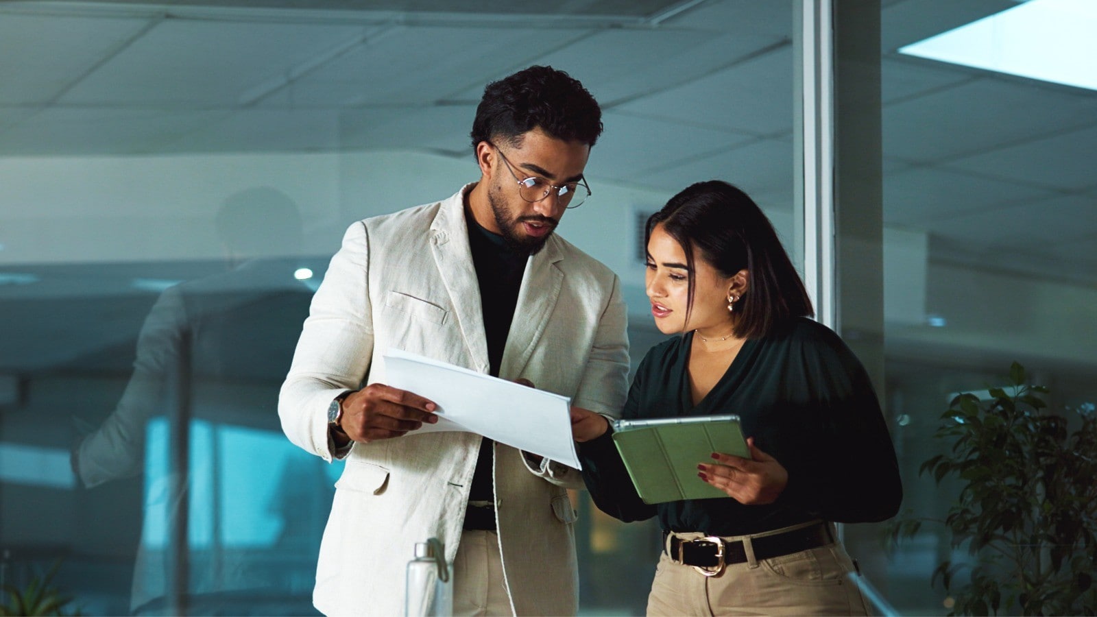 Two people looking at a document standing infront of an office meeting room