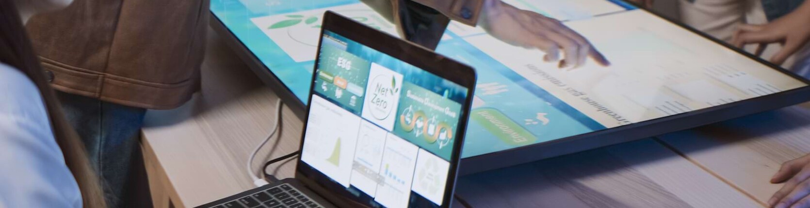 uz galda stāv laptops, kas projekcē saturu uz lielā ekrāna