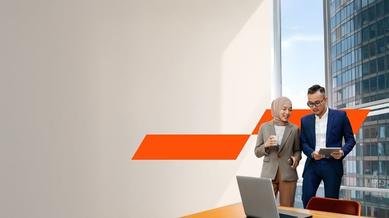 Two business professionals having a conversation in front of a glass window, one is holding the ipad while the other one is holding a coffee cup