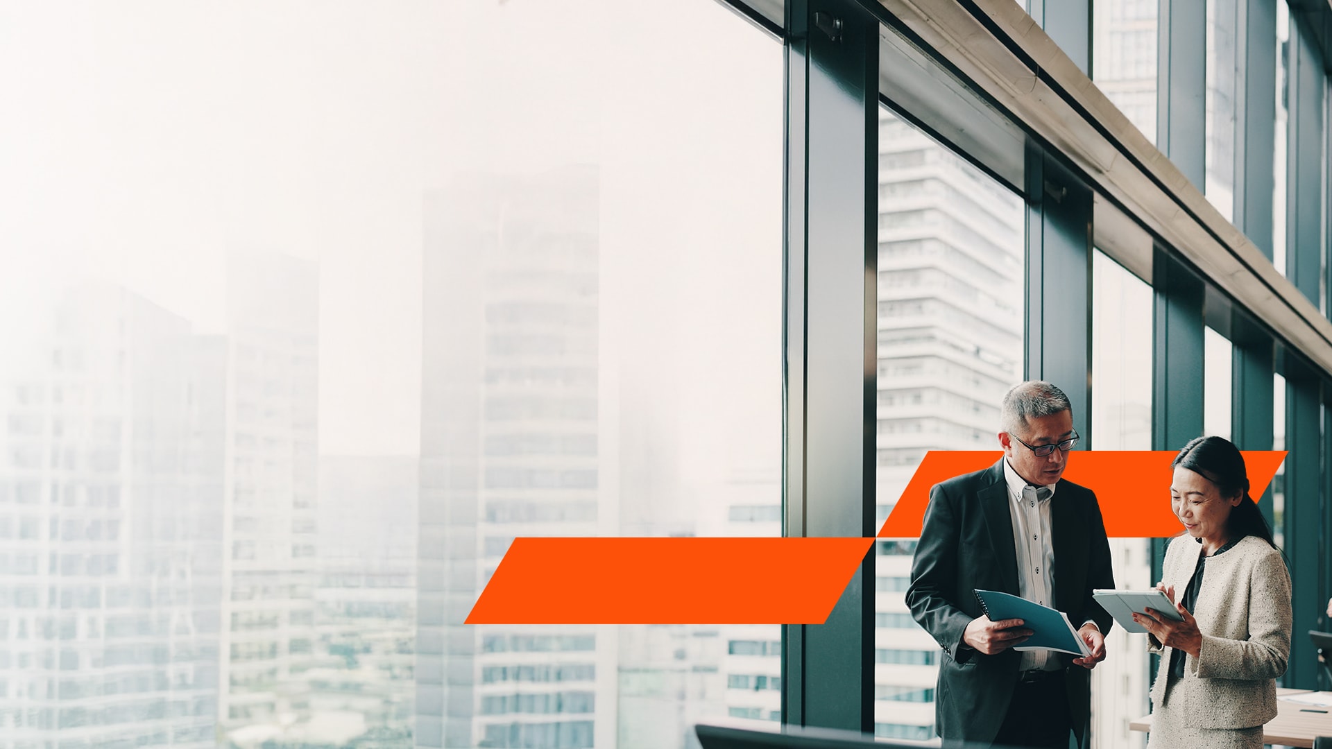 Two colleagues talking to each other near glass panel in office