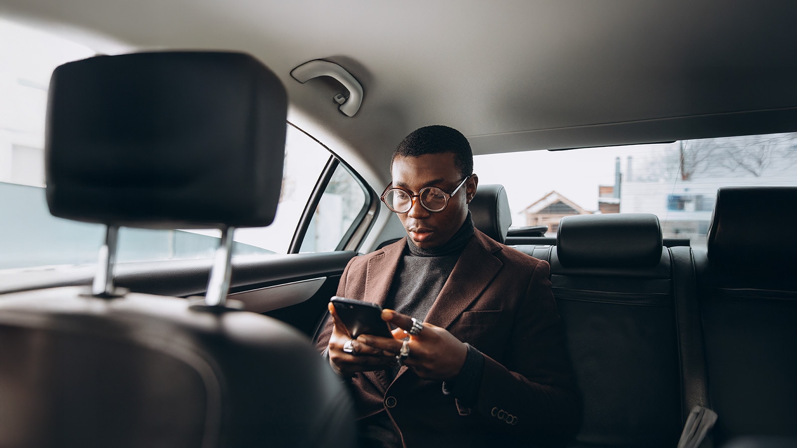 Young smiling african man using smartphone while sitting on backseat in car. Concept of happy business people traveling.