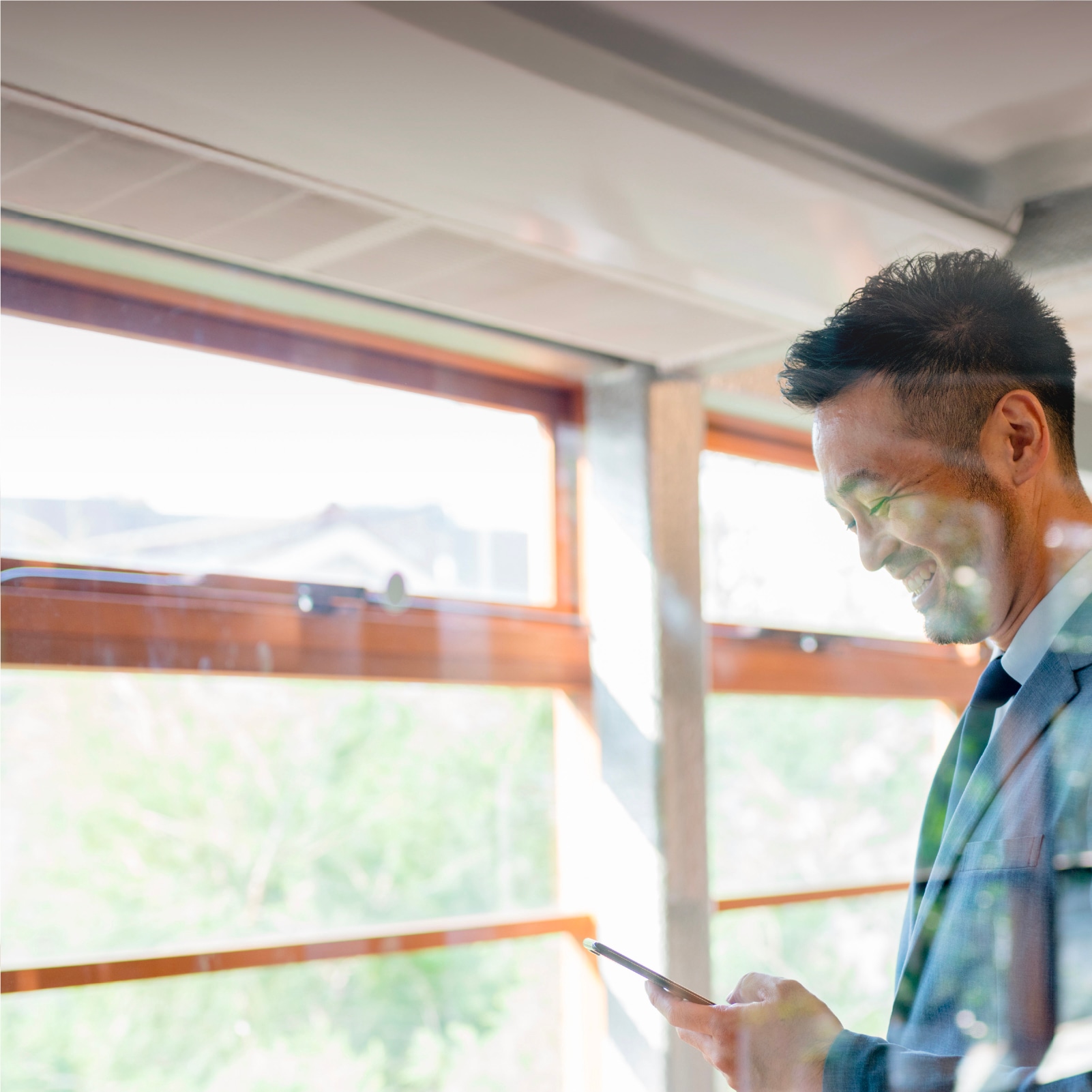 man looking at mobile phone next to the window